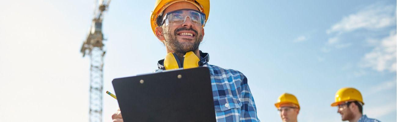 54720292 - business, building, paperwork and people concept - happy builder in hardhat with clipboard and pencil over group of builders at construction site